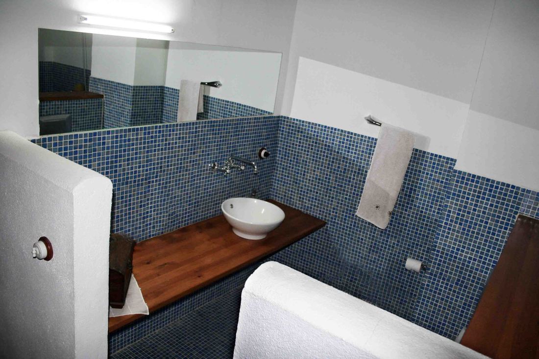A bathroom with blue mosaic tiling, a wall-mounted tap and a round vessel sink on a wooden counter