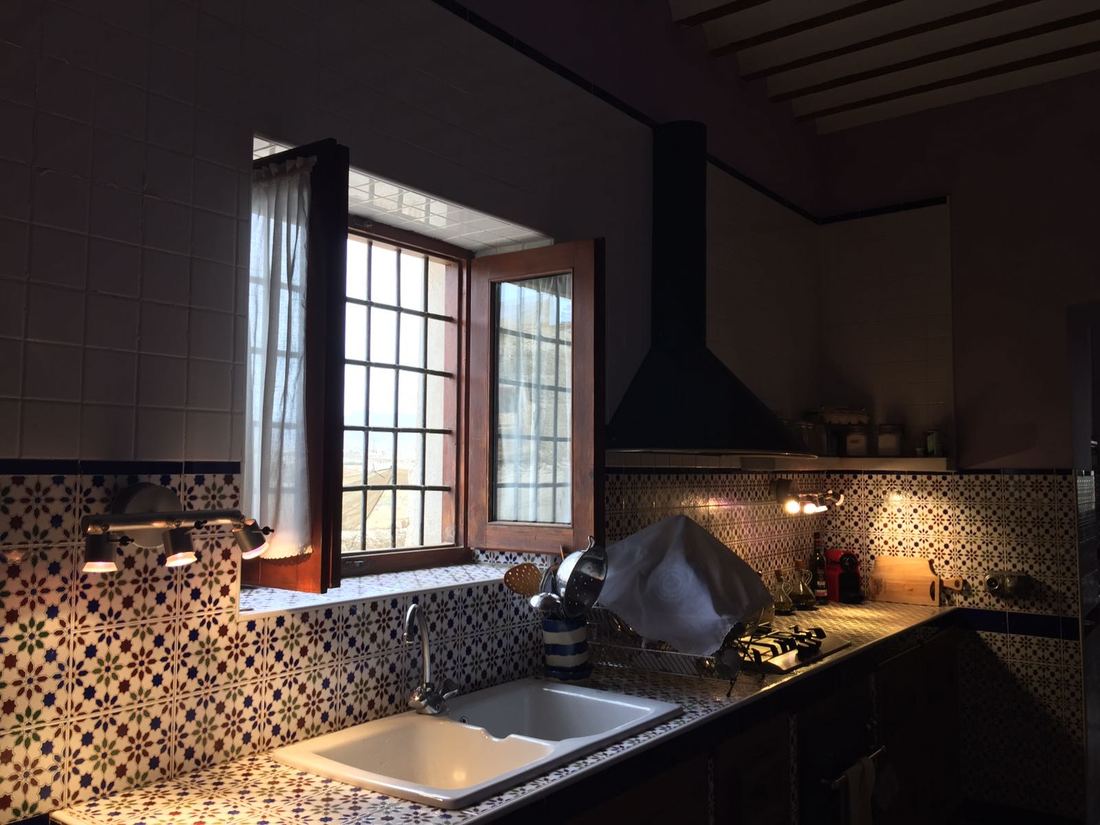 The kitchen, with hand-painted tiled walls, a gas hob and an open window looking out over the countryside