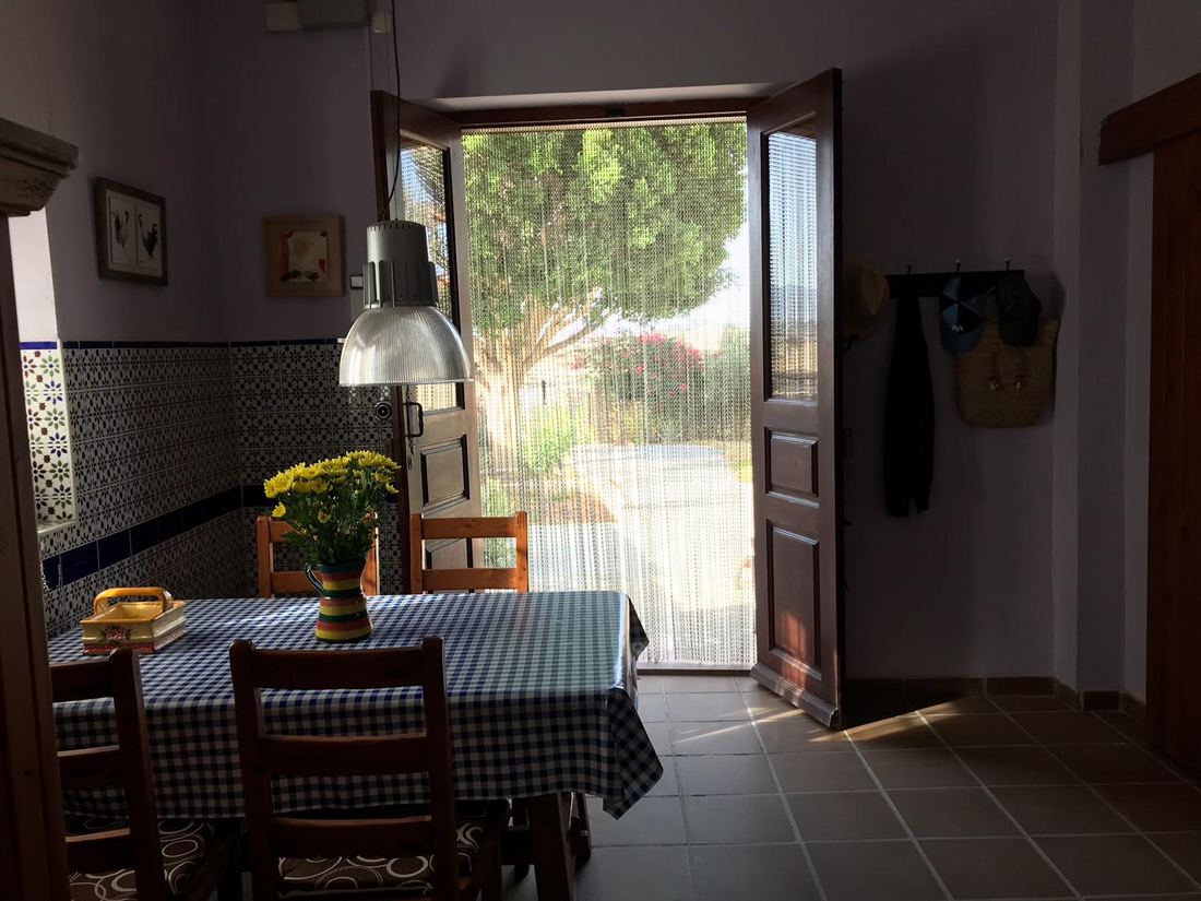 A small dining nook off the kitchen with a checked tablecloth and a door open to the garden