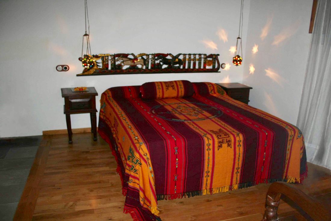 A bedroom with a colourful woven bedspread and a carved wooden wall hanging above the headboard