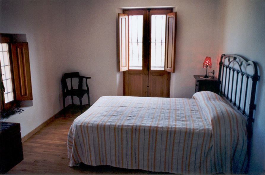 A bedroom with a wrought-iron bed frame and wooden shutters open to the light