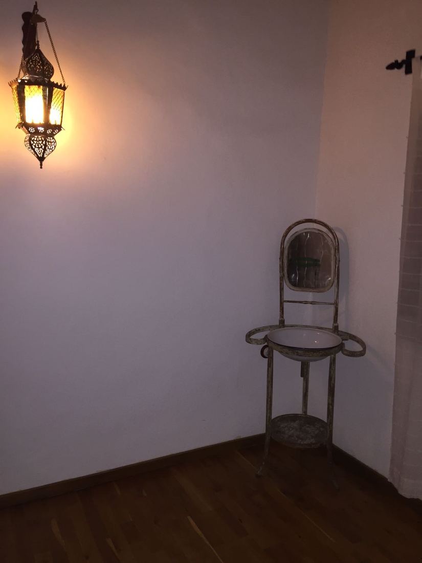 A bedroom corner with a vintage wash-stand, mirror and basin lit by an ornate hanging lamp