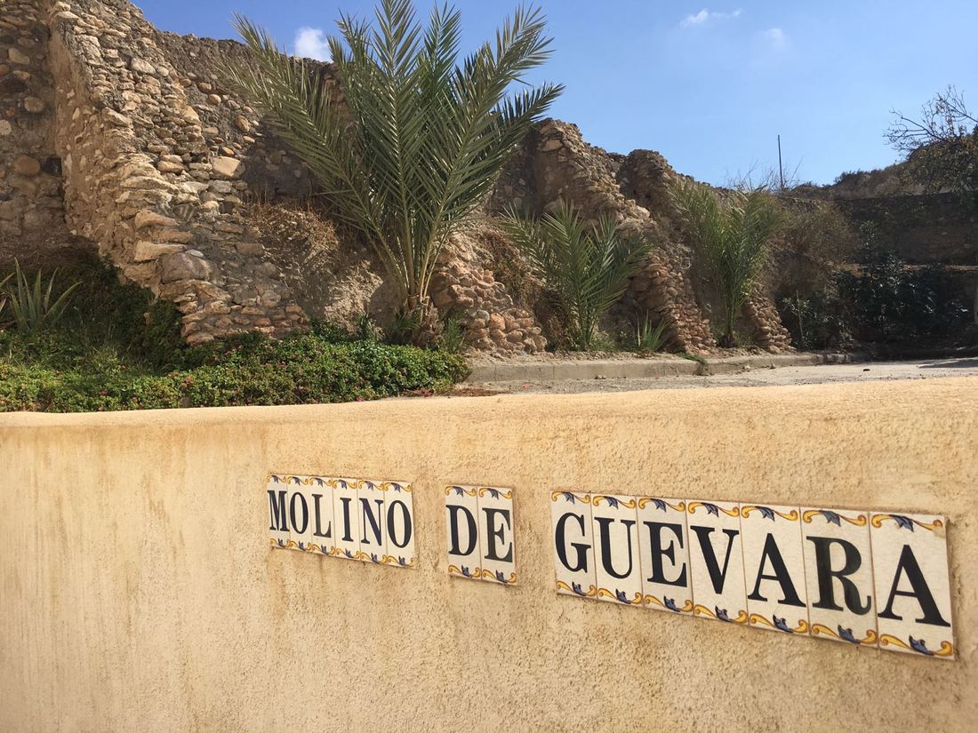 A ceramic tile sign reading Molino de Guevara, set into a garden wall beneath the ruined old acequia