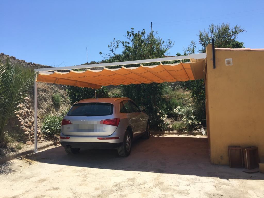 A car parked in the shade beneath a retractable awning beside the house