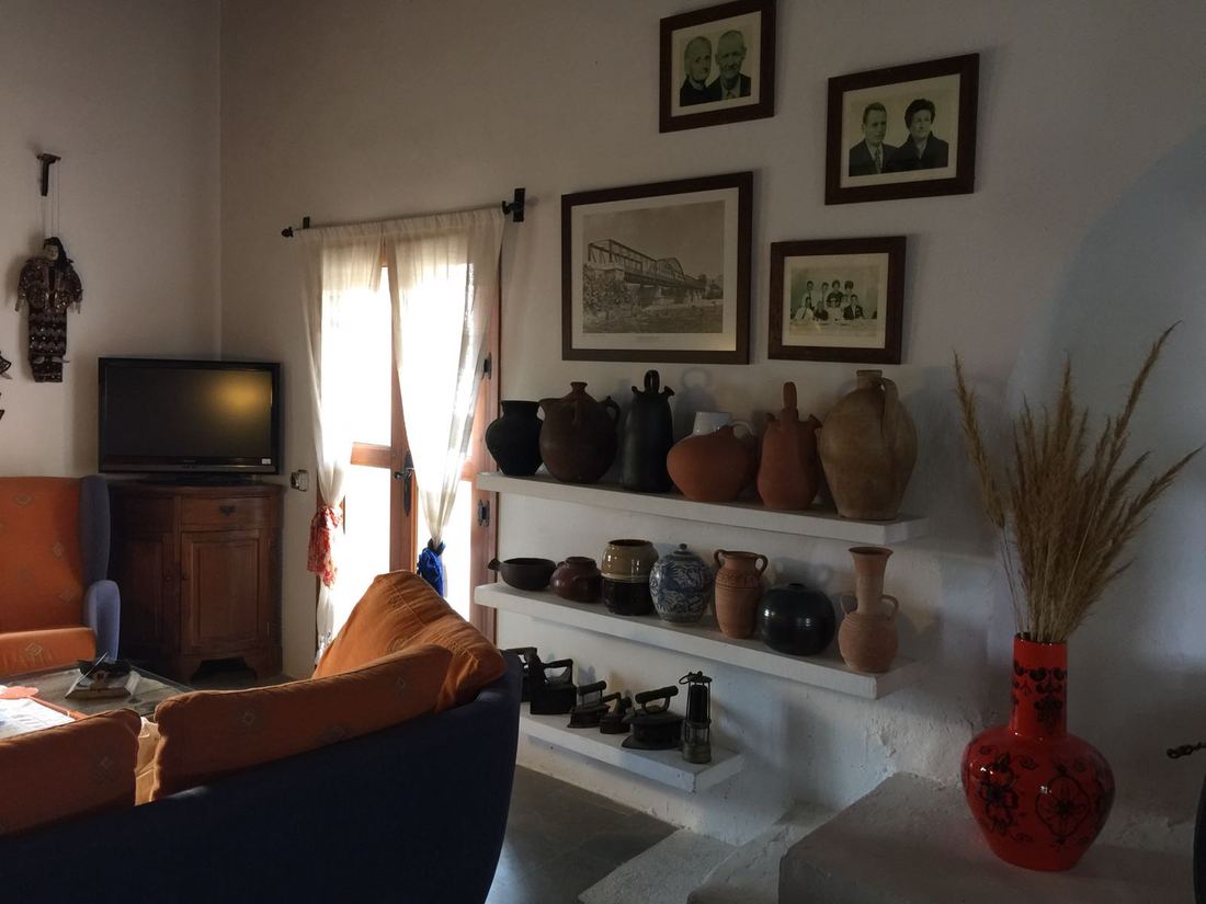 A corner of the living room with shelves of antique pottery jugs and family photographs